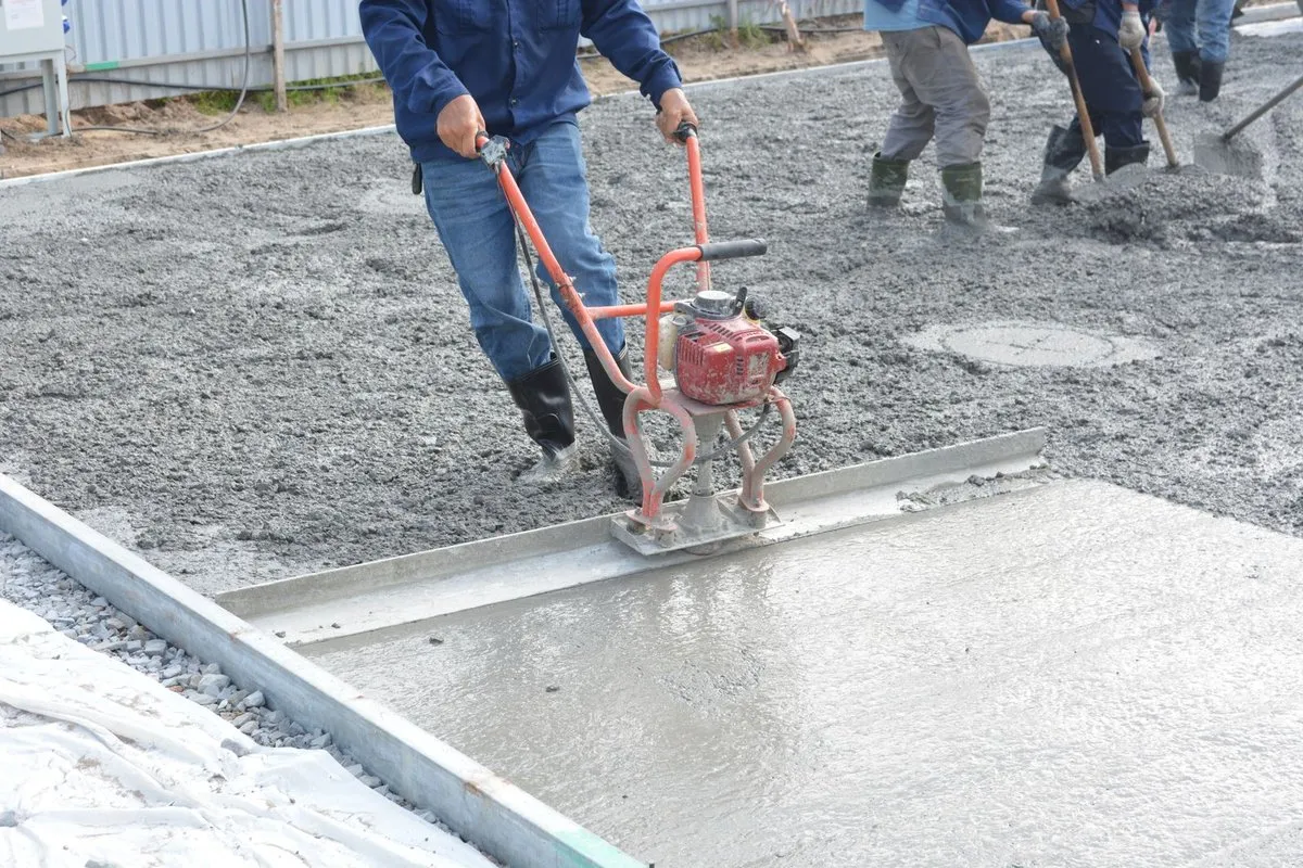 Worker screeding and leveling sand bedding for paver installation
